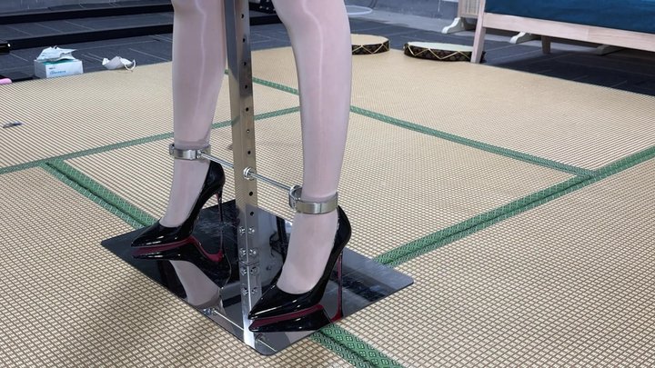 Asian woman bound by metal braces, high heels, shackles, handcuffs, experiencing