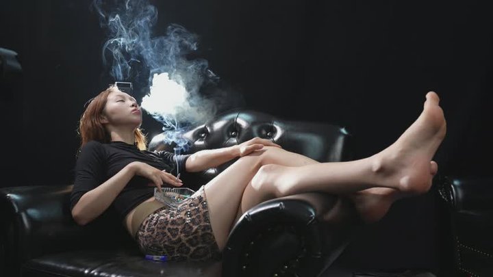Sensual Smoking Performer Lounging Barefoot on Leather Couch Exhaling Smoke — TI